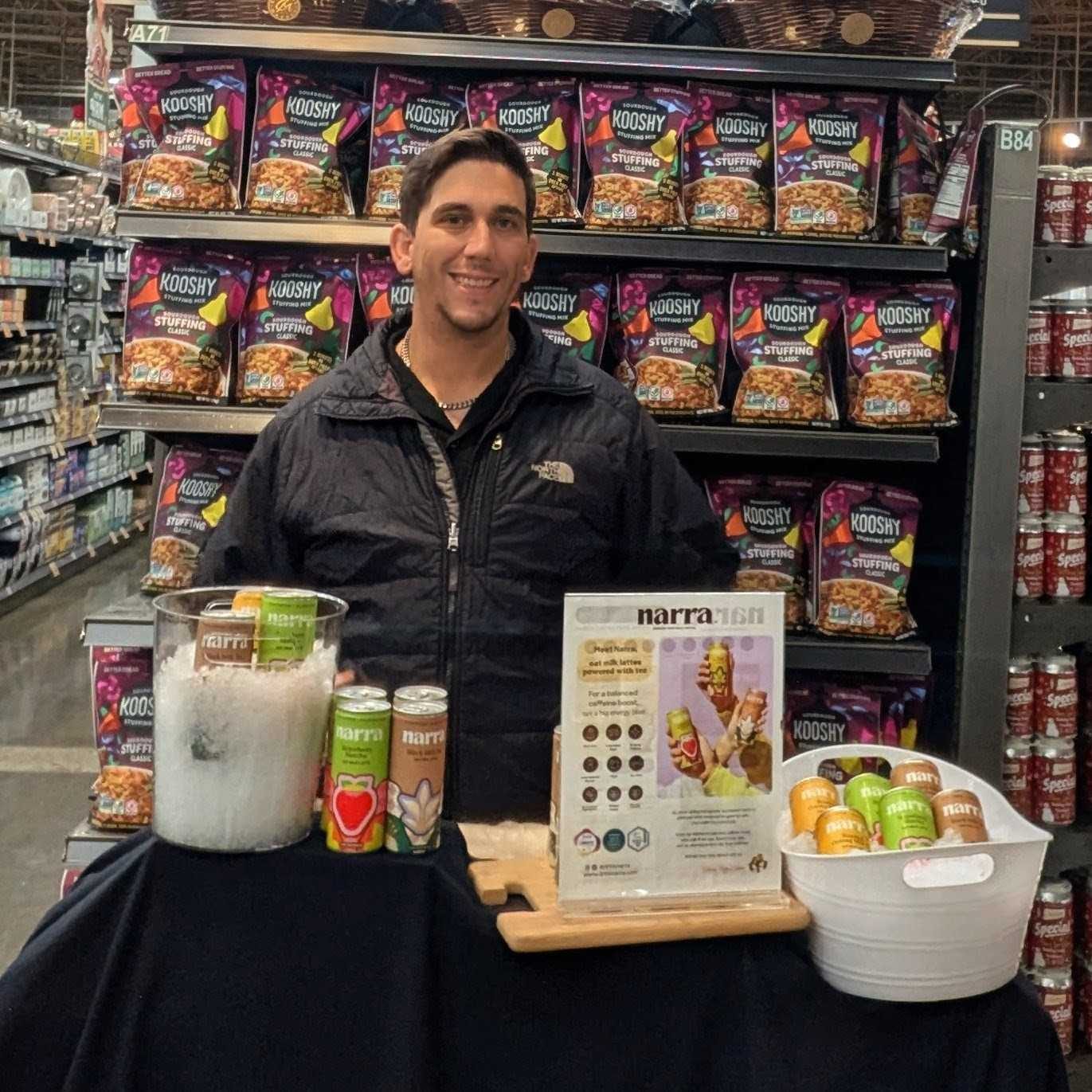 A staffed sampling table set up in a grocery aisle, with product displayed and drinks poured ready to hand out.