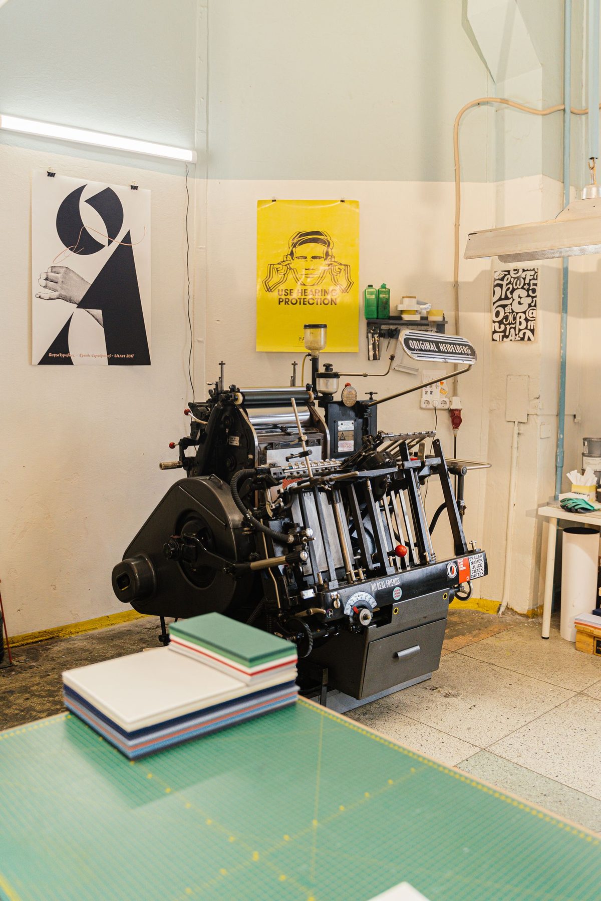 A print room with a press, stacked paper and finished posters pinned to the wall.