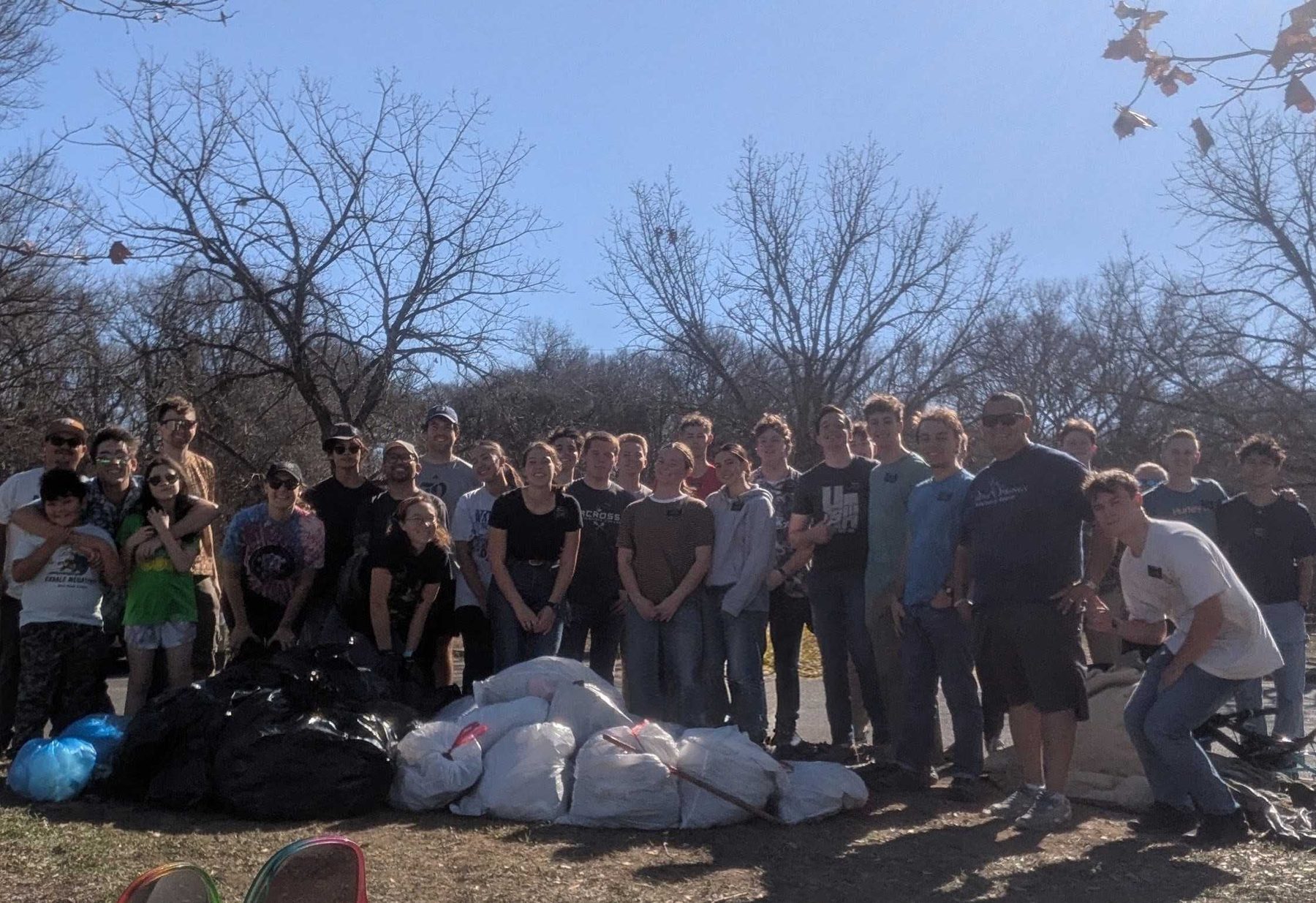 A group of volunteers gathered behind piled bags of collected litter, with bare winter trees behind them.