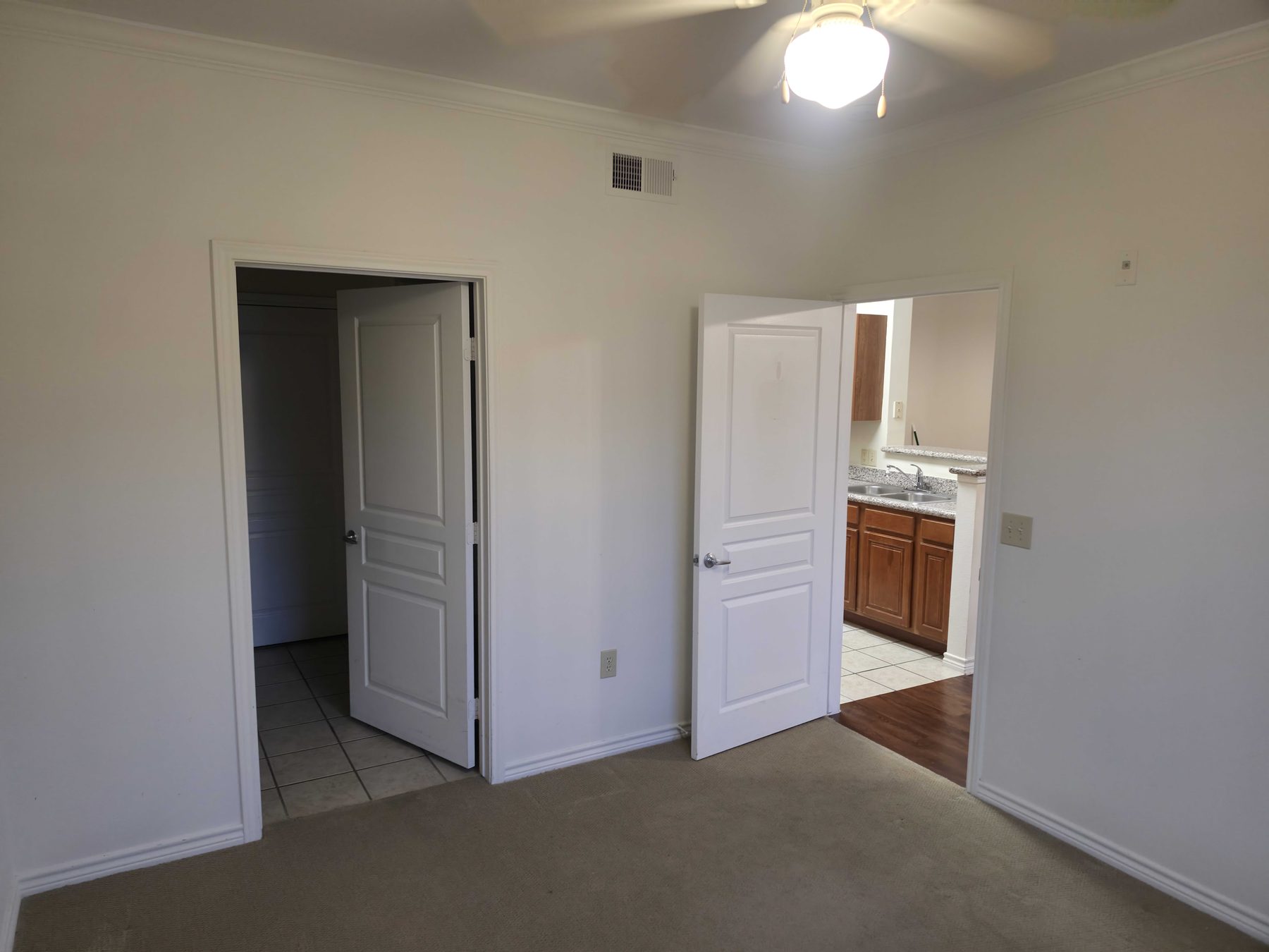 A cleared room with doors open through to a kitchen beyond.