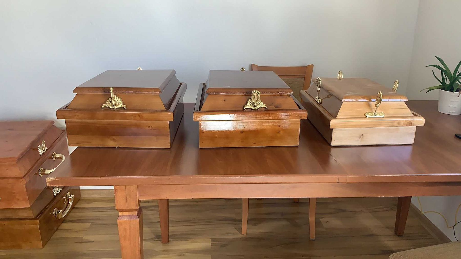 Small finished timber caskets with brass fittings, set out together on a dark wood table.