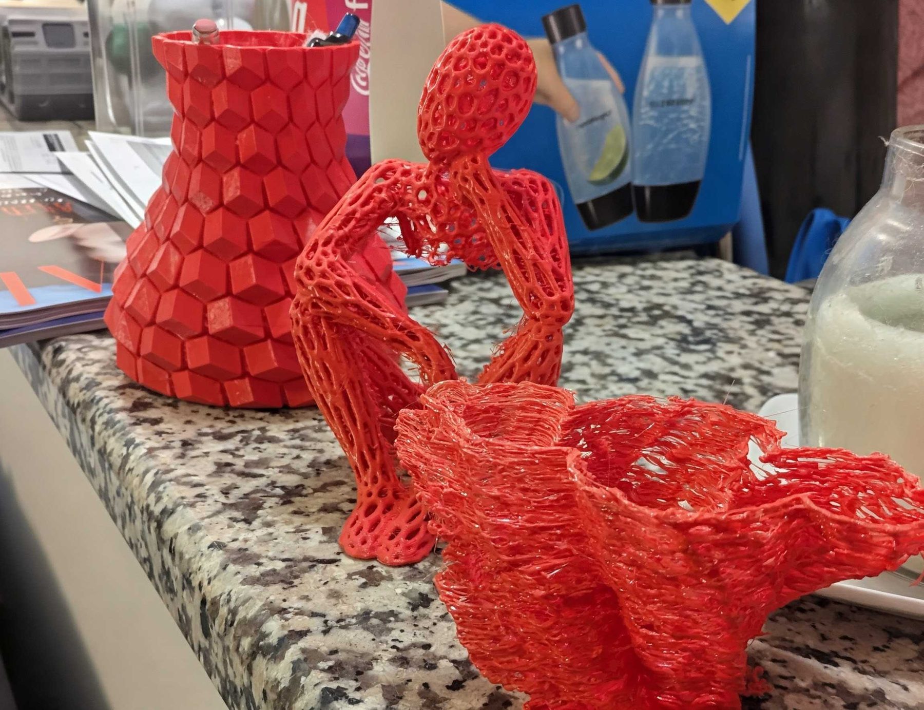 Several finished 3D printed vessels grouped on a table, one solid red and one open latticework.