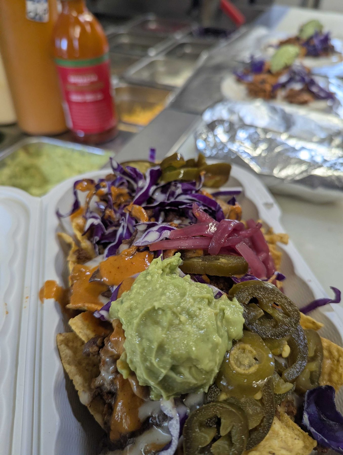 A loaded plate of food with guacamole, slaw and tortillas, photographed close on a serving table.