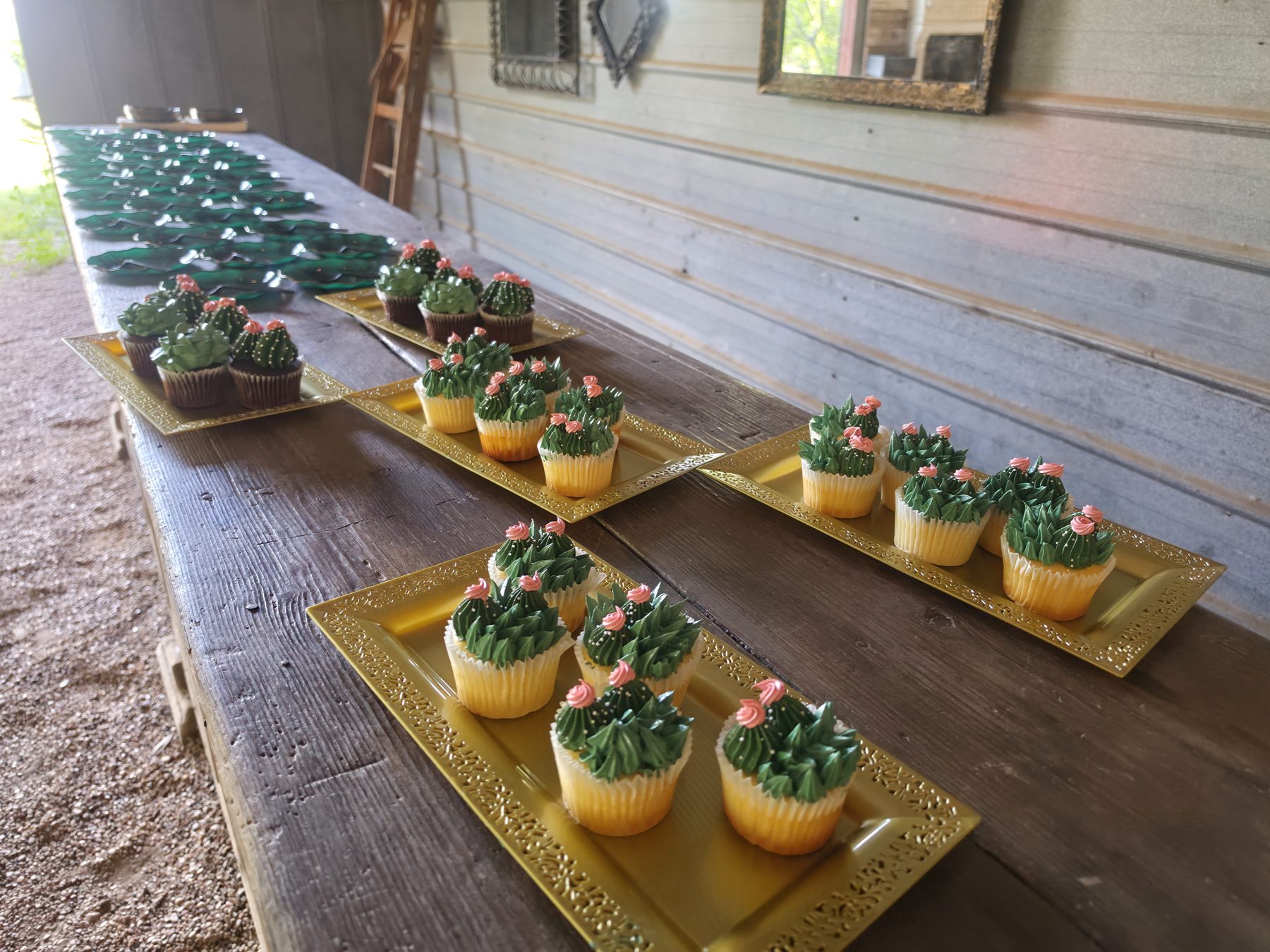 Trays of decorated cupcakes laid out along a timber table at an outdoor venue.
