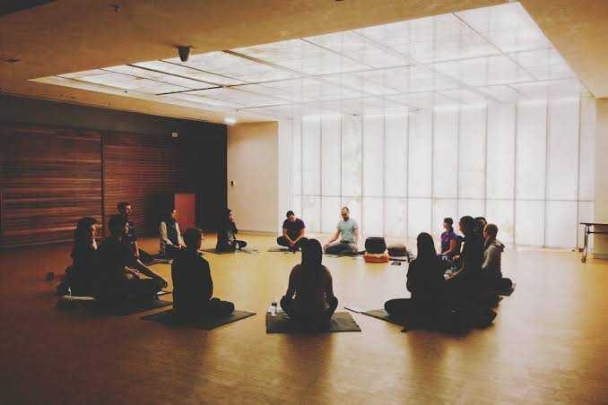 A circle of people sitting on the floor of a plain, bare room.