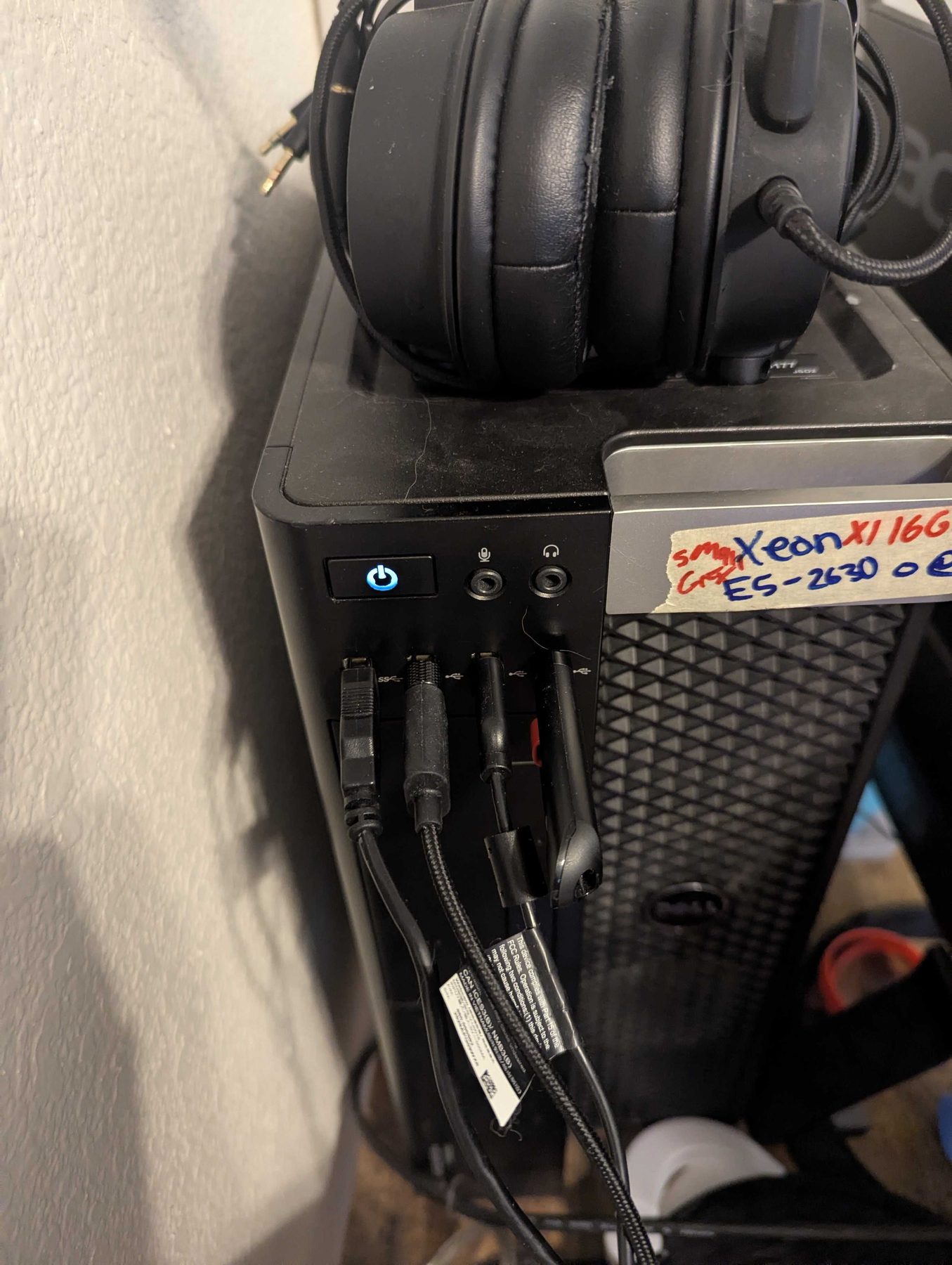 A black desktop tower with headphones resting on top and cables running from its ports, a strip of masking tape on the front with the processor written on it by hand in marker.