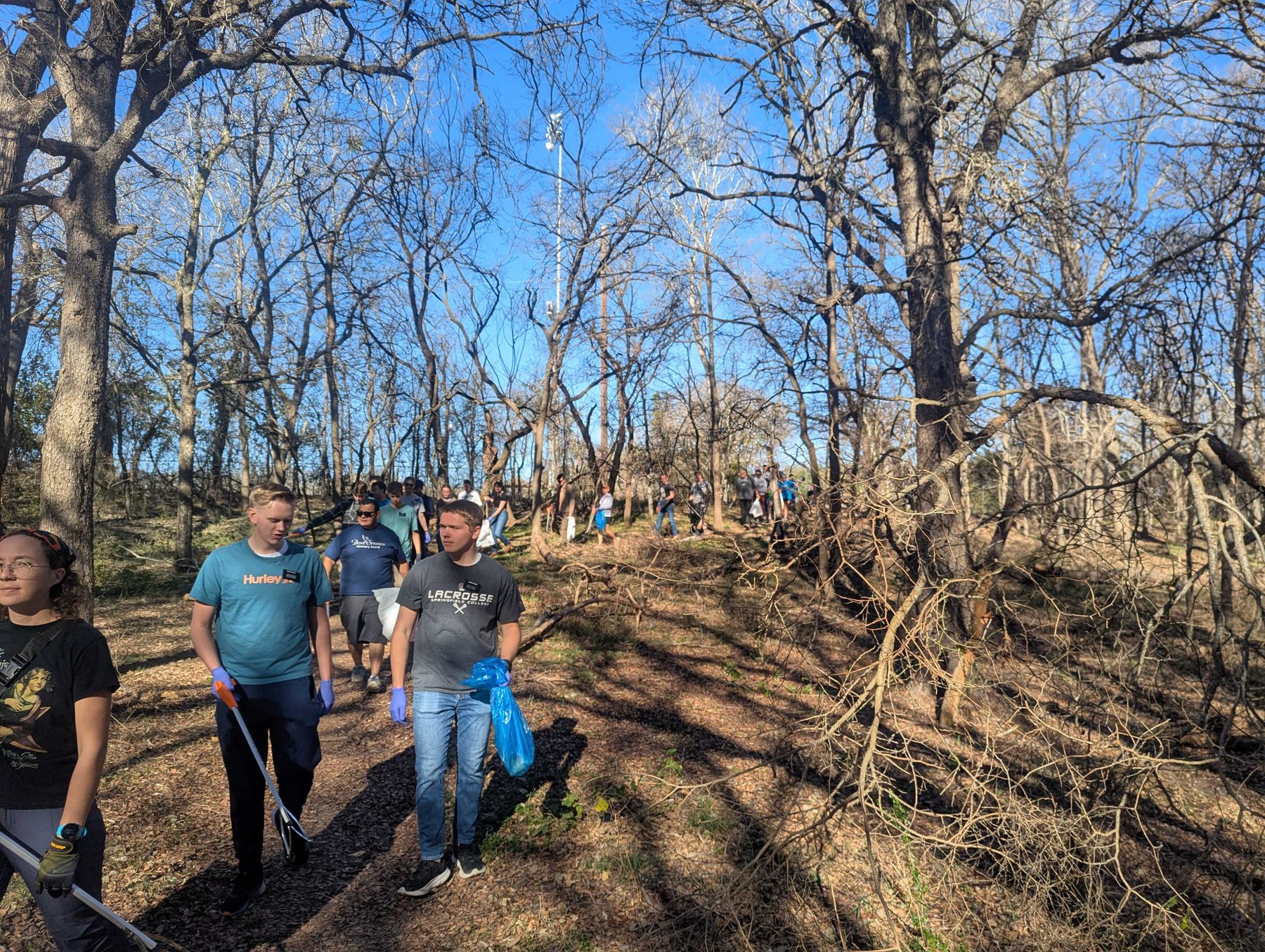 Volunteers walking a wooded trail out to a creek cleanup, carrying grabbers and collection bags.