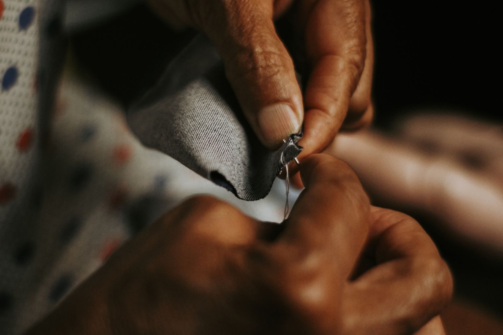 A pair of weathered hands working a piece of patterned fabric with a small tool.