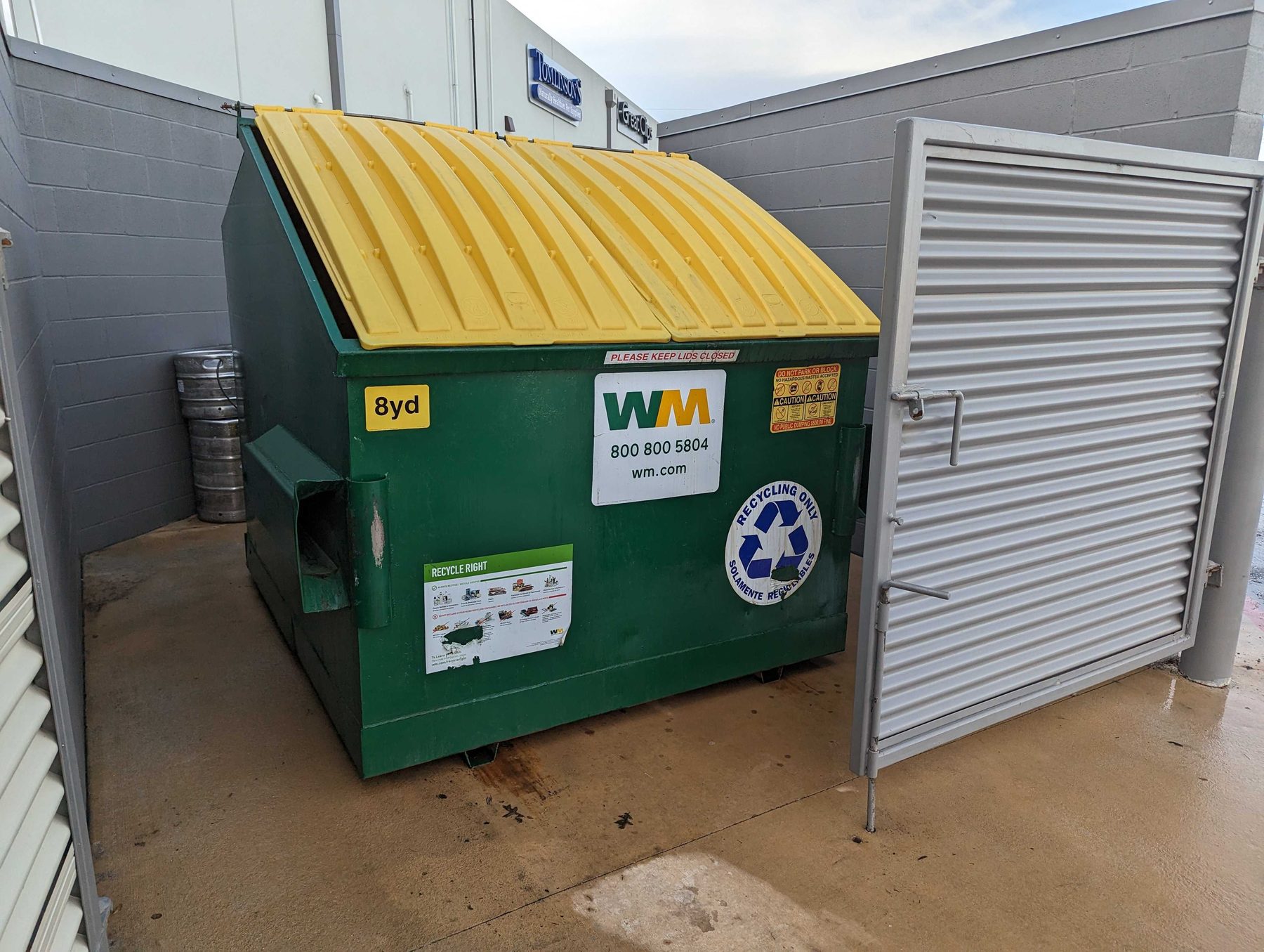 A commercial dumpster standing in a clean walled enclosure on a washed concrete pad.