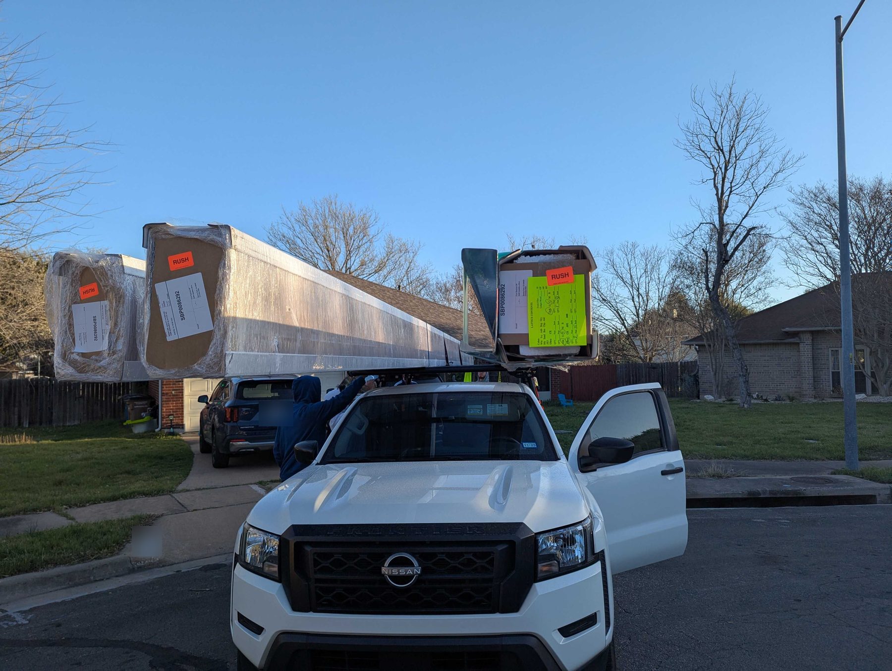 A pickup truck carrying long wrapped panels strapped above the cab, parked on a residential street.
